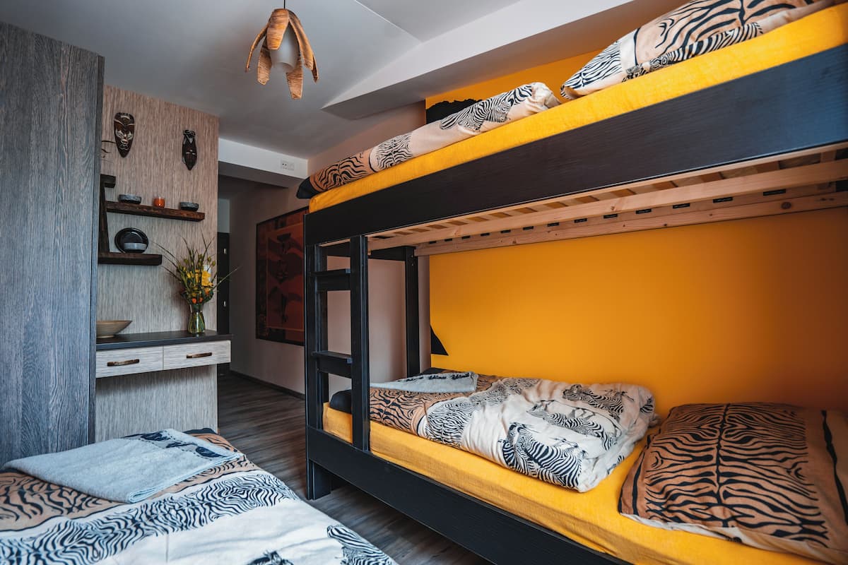 Un lit superposé avec une literie à motifs zébrés, un bureau en bois orné d’un vase de fleurs et une étagère murale décorative.