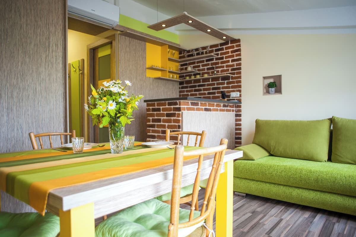 Un coin repas avec une longue table, des chaises, un vase de fleurs et un canapé vert.