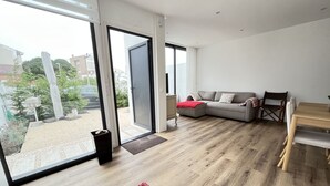 Ein modernes Wohnzimmer mit einem großen Schiebeglasfenster, einem grauen Sofa, einem Holzessttisch und einem roten Teppich.