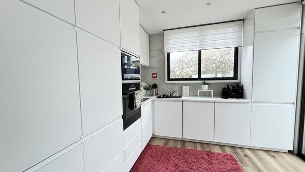 A modern kitchen with white cabinetry, a red rug, and a window with blinds. - Espinho Beach House by Trip2Portugal (Espinho)