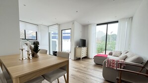 A modern living room with a wooden dining table, a sofa, and a TV on a cabinet. - Espinho Beach House by Trip2Portugal (Espinho)