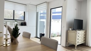 Ein modernes Wohnzimmer mit einem Holzesstisch, einem Fernseher auf einer Anrichte und Blick durch eine Glastür.