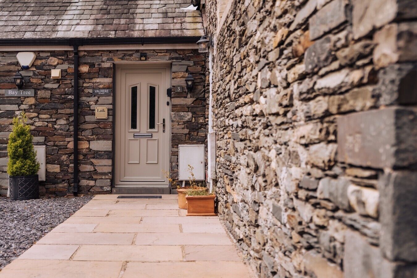 A stone building with a beige door, a small potted plant, and a sign that reads 'Bay Tree.'