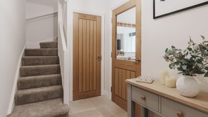 Un escalier menant à une porte en bois, une petite table avec une plante, des bougies et un miroir.