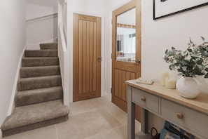 A staircase leading to a wooden door, a small table with a plant, candles, and a mirror. - Valmere Retreat, Luxury Cottage, Windermere (Windermere)