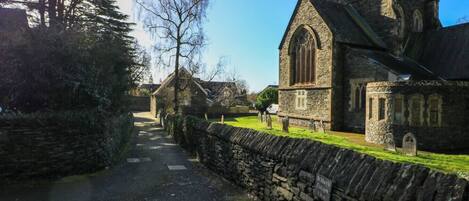 En stensatt gång leder fram till en kyrka med ett högt torn och en mindre byggnad med en skylt där det står ”Graham’s Cottages”.