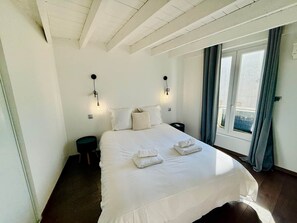 Une chambre d’hôtel avec un grand lit, deux tables de chevet, une fenêtre avec des rideaux et un plafond avec des poutres apparentes.