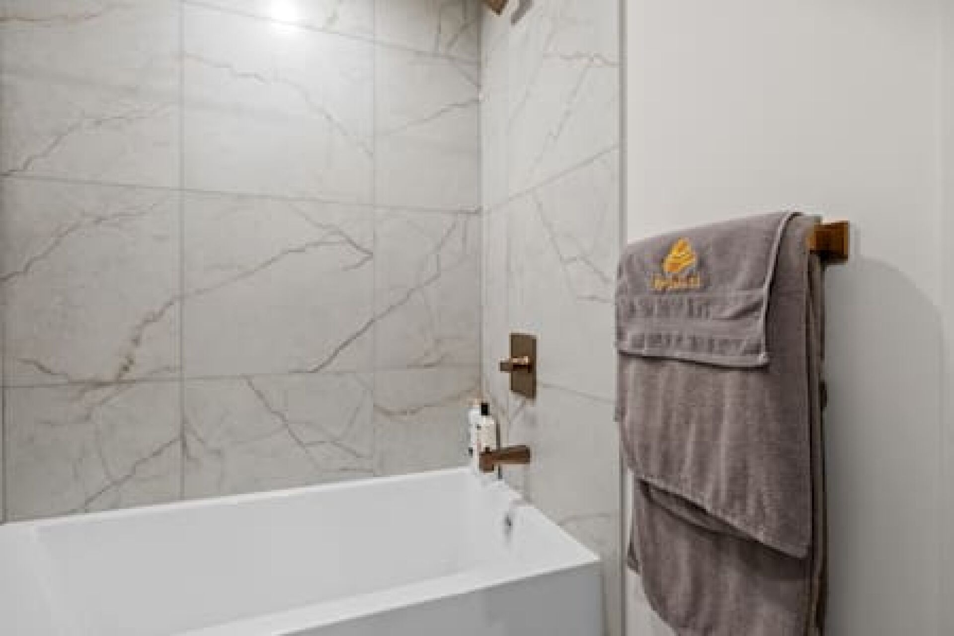 Een badkamer met een witte badkuip, marmeren wanden en een handdoek aan een houten rek.
