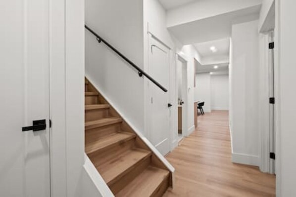 A modern interior with a wooden staircase, white walls, and a hallway leading to another room. - "Pavia" Suite, Private Entry, Short Walk to U of C (Calgary)