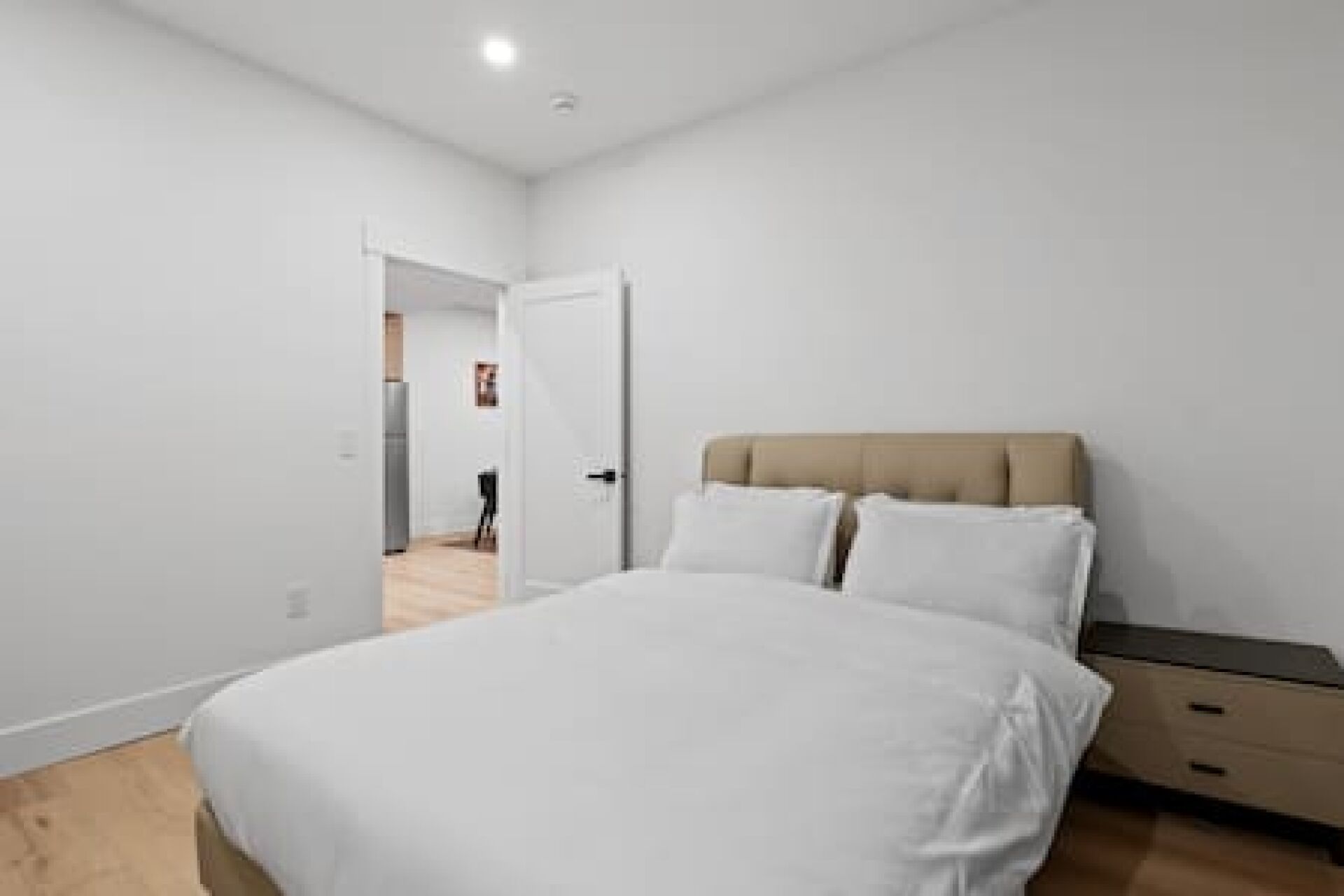 A bedroom with a bed, a nightstand, and a door leading to a hallway.