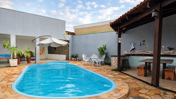 A swimming pool with stone tiles, white outdoor furniture, and a bar area. - Vacation Home - Recanto Flor de Laranjeira, Palmas-Tocantins. (Palmas)