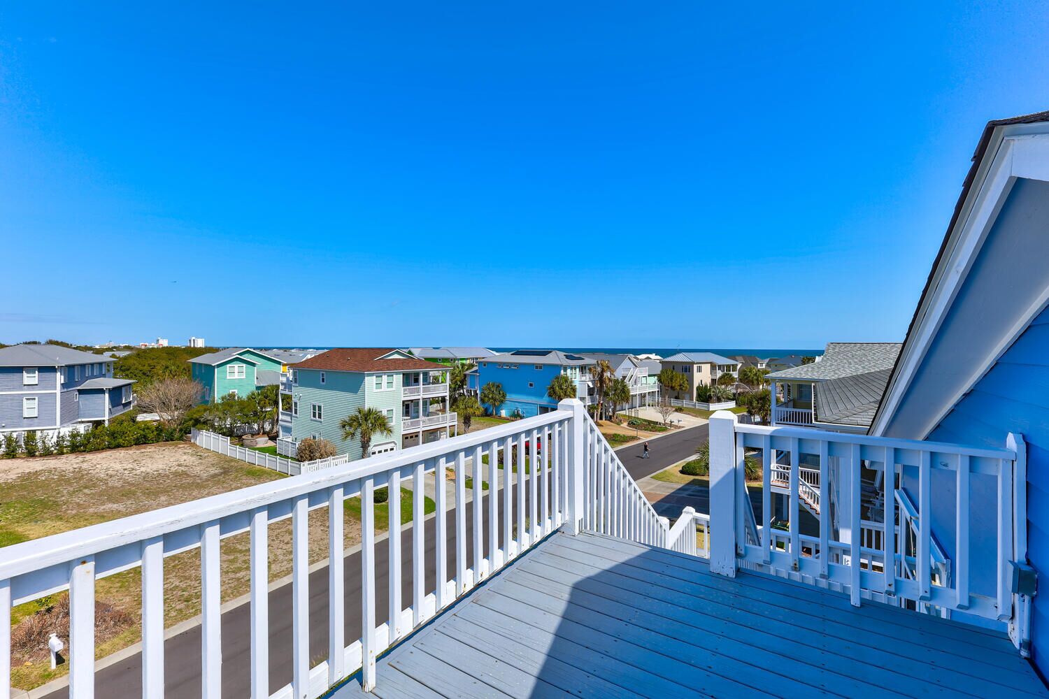 Spacious deck with white railings overlooking colorful coastal neighborhood and blue skies.