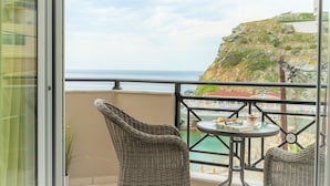 A balcony with wicker chairs, a small table, and a view of the sea and a rocky hill. - Cretan Experiences Sea View (Malevizi)