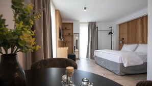 Hotellihuone, jossa on sänky, televisio, työpöytä tuolilla ja huonekasvi.