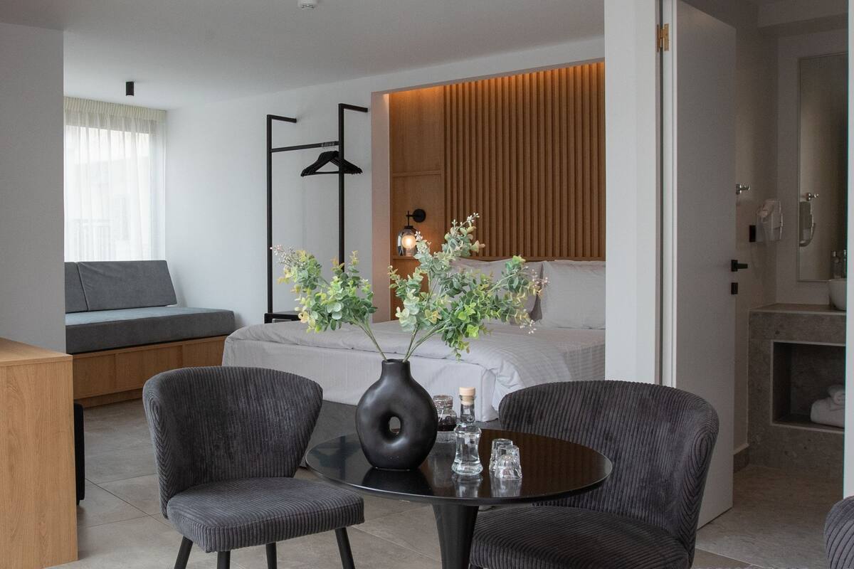 Ein modernes Hotelzimmer mit Bett, Sitzbereich, Esstisch und Bad.