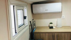 Et lille værelse med seng, et lille bord, en stol, et vindue, en aircondition og et skab.