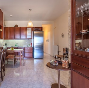 A modern kitchen with wooden cabinets, a stainless steel refrigerator, and a dining area with a table and chairs. - Elena s Apartment Near the Beach (Hersonissos)