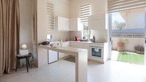 A modern kitchen with a dining area, a small table with a lamp, and a view of the outside. - The Fifty Condo in Heraklion City Center (Heraklion)