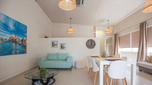 A modern living room with a sofa, dining table, chairs, a coffee table, and a painting of a cityscape. - The Fifty Condo in Heraklion City Center (Heraklion)