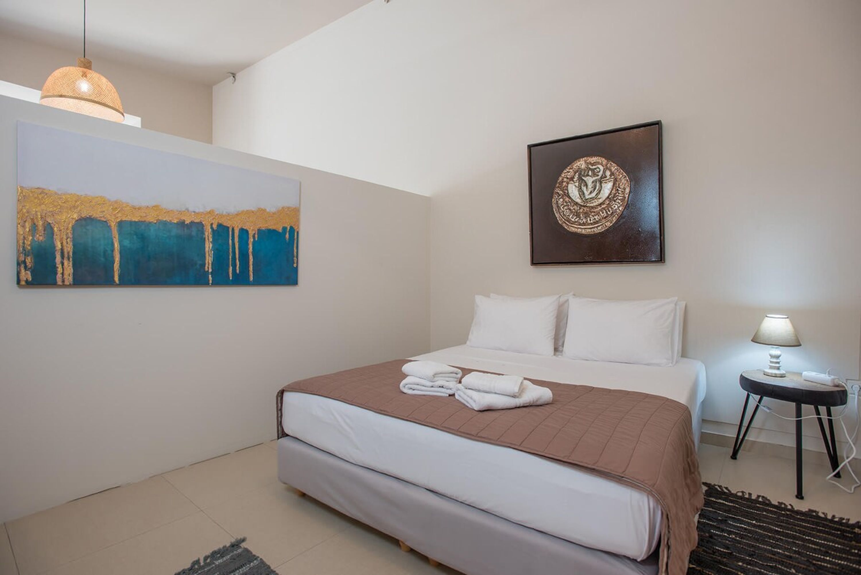 Una habitación de hotel con una cama, un cuadro, un emblema enmarcado, una lámpara y una alfombra.