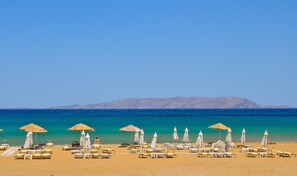 A beach with sun loungers and umbrellas, a clear sky, and distant mountains. - Meraki Beautiful Apartment Near the Sea (Malevizi)