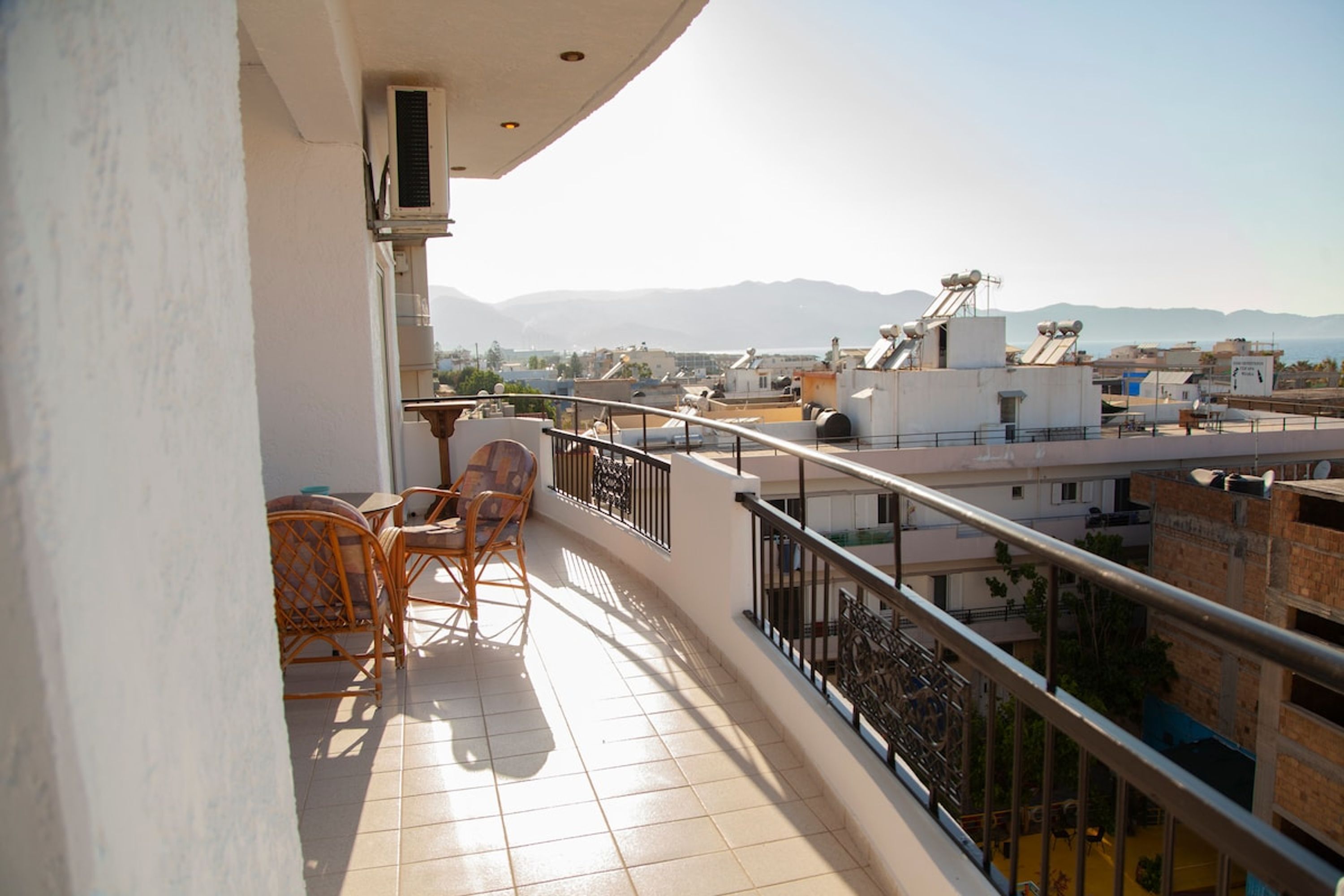 Un balcone con tavolo e sedie, una ringhiera e vista su edifici e montagne.