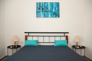 Ein Bett mit einer dunkelblauen Decke, zwei türkisfarbenen Kissen, einem schwarzen Kopfteil und einem an der Wand hängenden Kunstwerk mit Text.