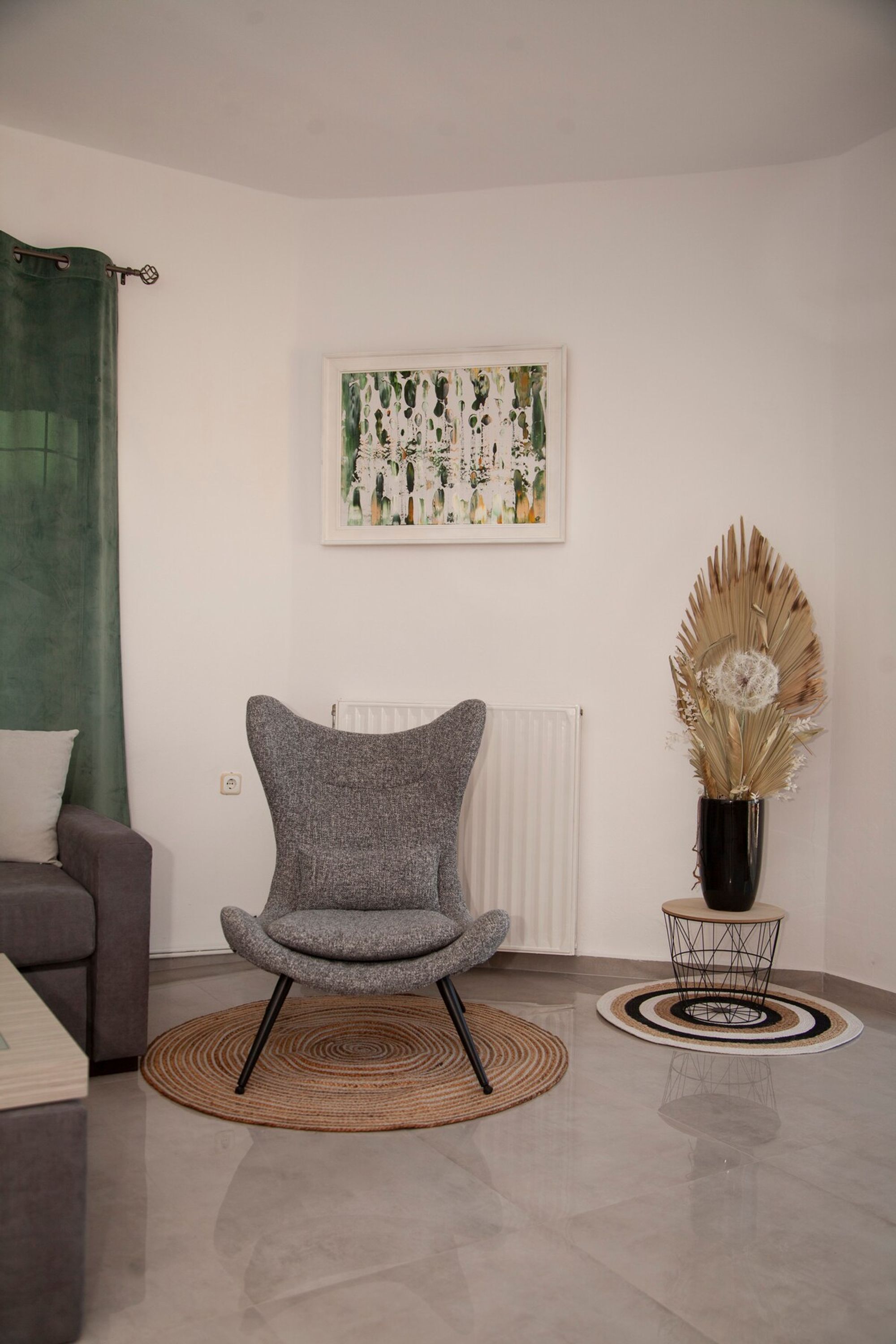 A modern living room with a grey armchair, a round rug, a framed artwork, and a decorative vase.