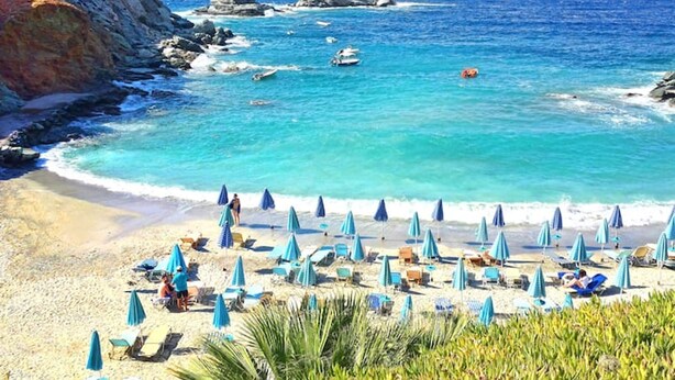 Een strand met parasols, stoelen en rotsachtige kliffen.
