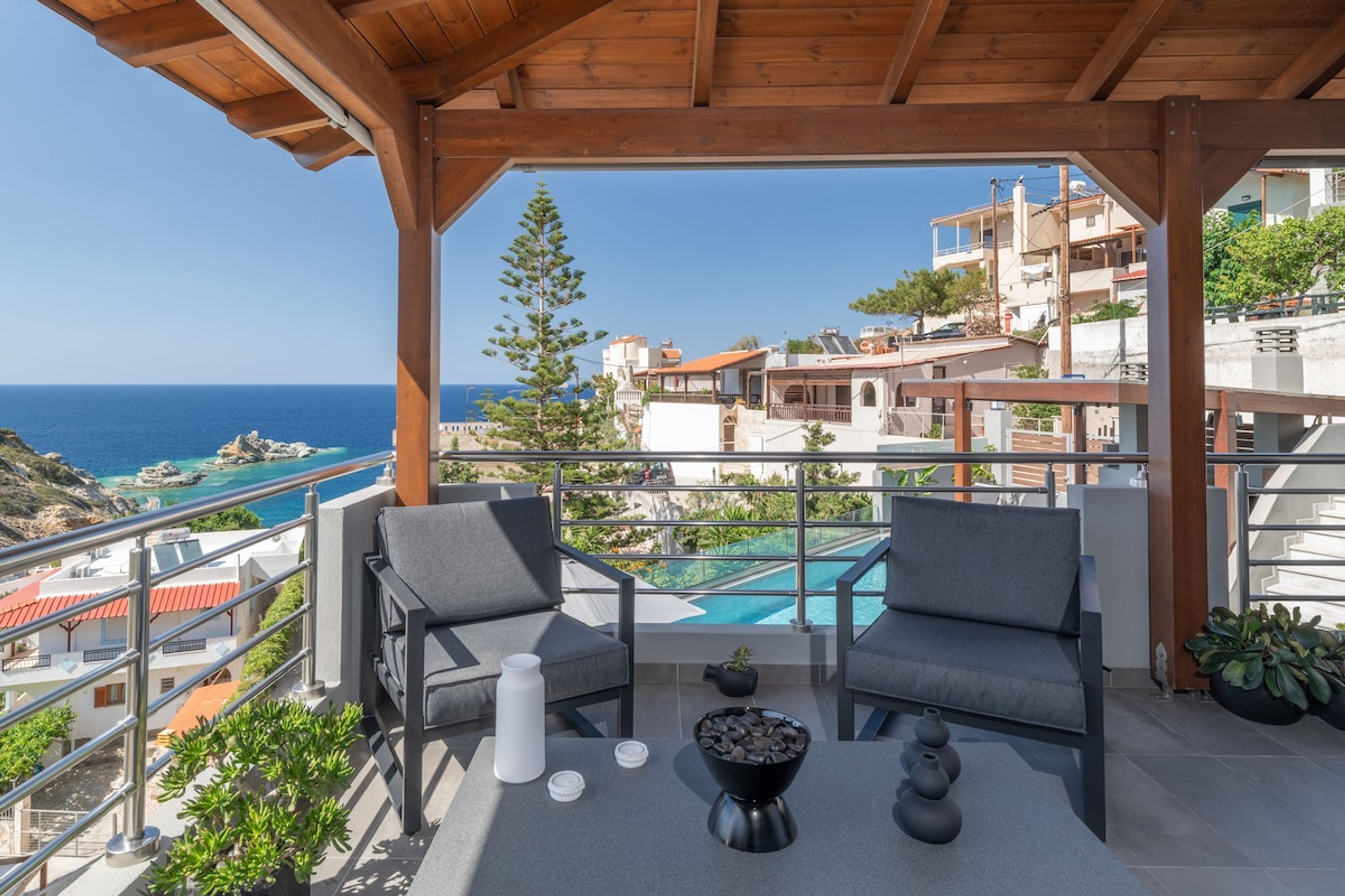 A balcony with two chairs, a small table, and a view of a swimming pool and buildings.