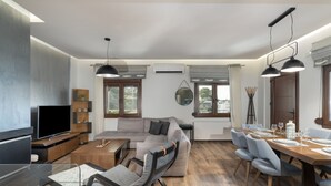 Een moderne woonkamer met een bank, een eettafel, een televisie en een groot raam.