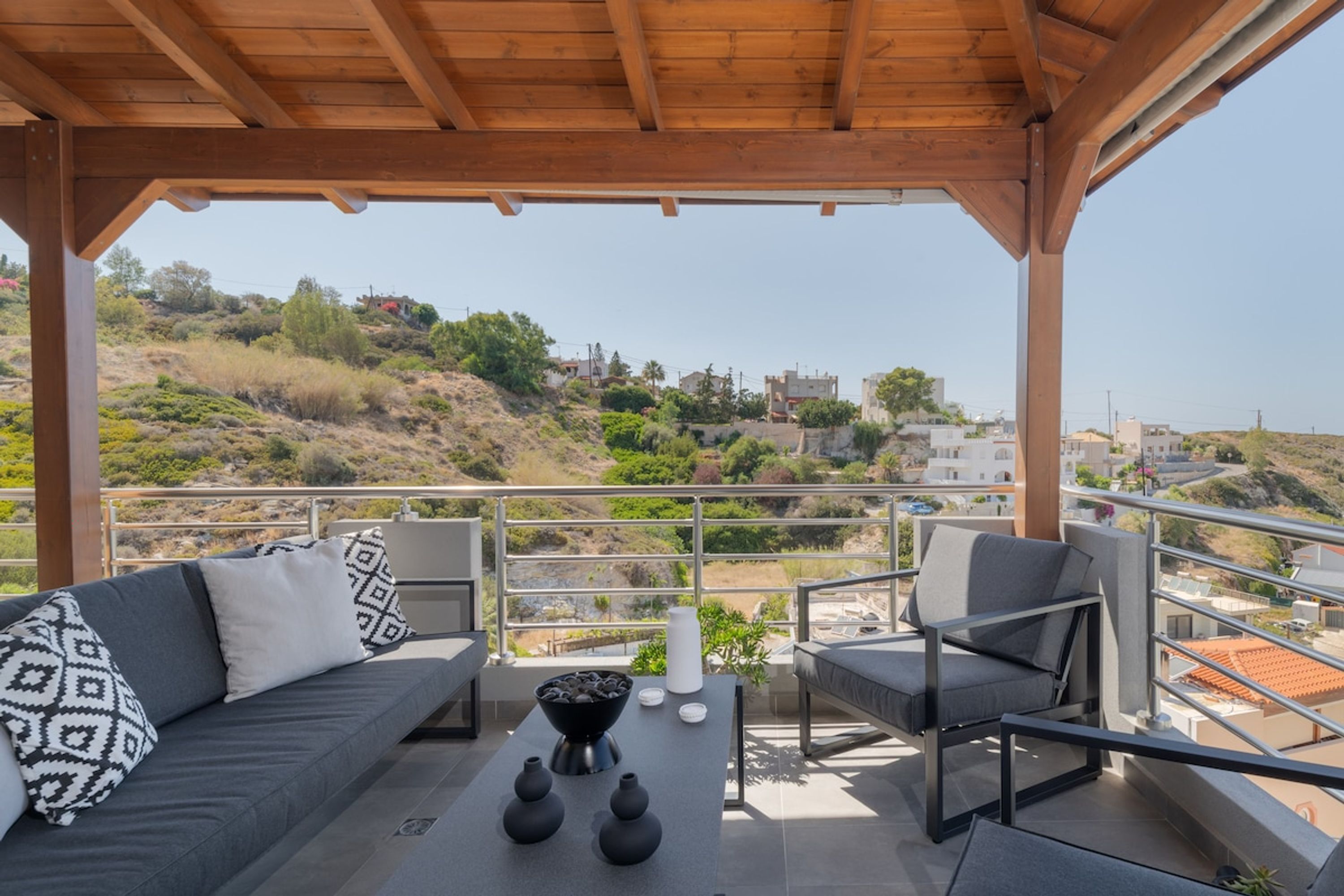 A covered outdoor seating area with a sofa, chairs, and a table with vases.