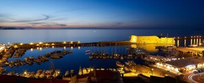A harbor at dusk with boats docked, a fortified building, and a marina with lights. - Havana 2 Sea and Pool Apartment (Malevizi)