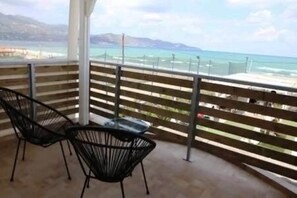 Un balcon avec deux chaises et une table, donnant sur une plage et l’océan.