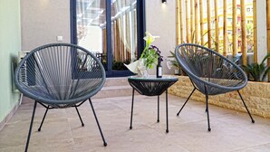 A patio area with two black wire mesh chairs, a small round table with a vase of flowers, and a bottle of wine. - Havana 3 Sea and Pool Apartment (Malevizi)