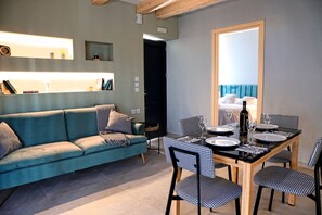 Ein modernes Wohnzimmer mit einer Couch, einem Esstisch, Stühlen und einem Spiegel, der ein Bett reflektiert.
