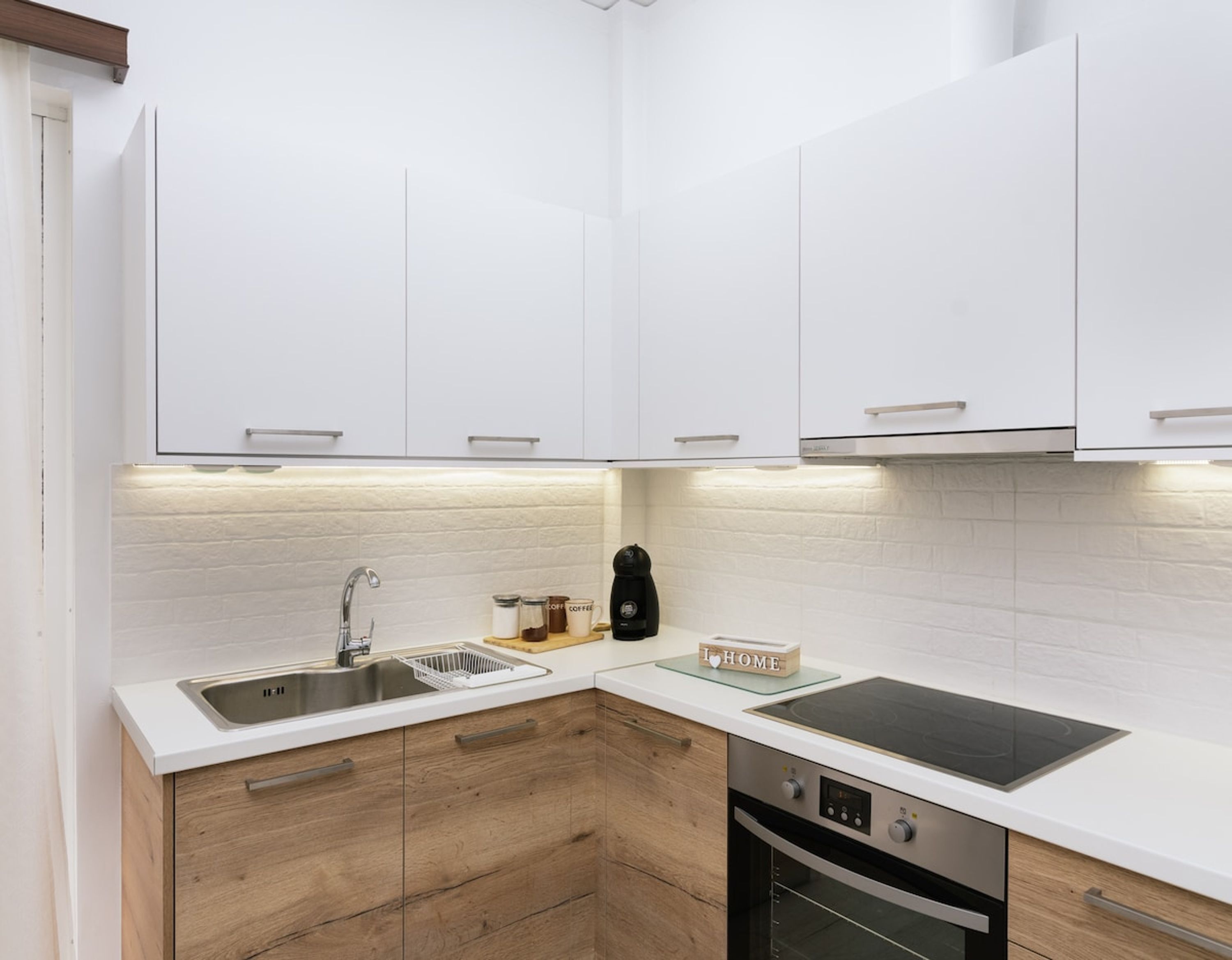 Una cocina moderna con armarios blancos, un lavamanos de acero inoxidable, una cafetera y un horno empotrado.