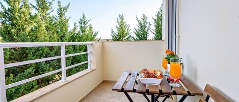 A balcony with a table set for breakfast, a bench, and a view of trees.