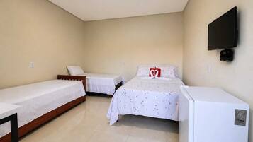 A hotel room with two single beds, a small table, a TV mounted on the wall, and a white refrigerator.