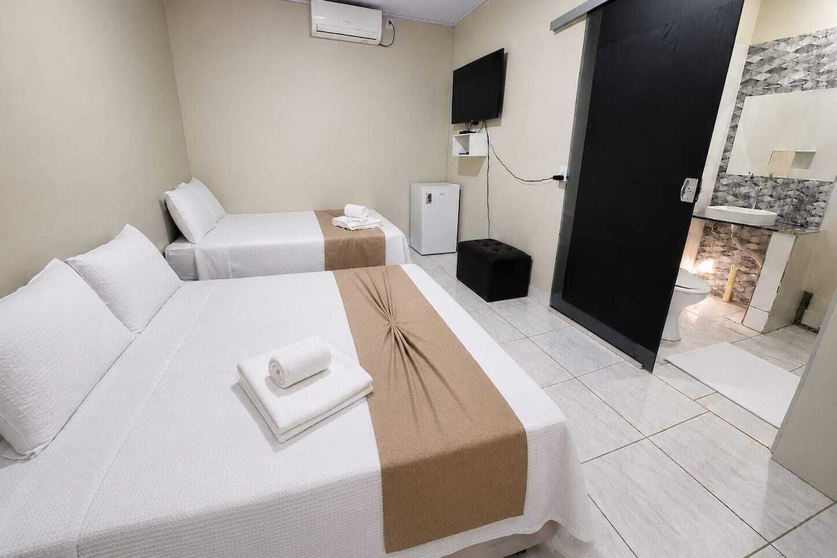 A hotel room with two beds, a TV, a minibar, and a bathroom visible through an open door.