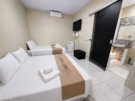 Habitación de hotel con dos camas, televisión, minibar y baño visible a través de una puerta abierta.