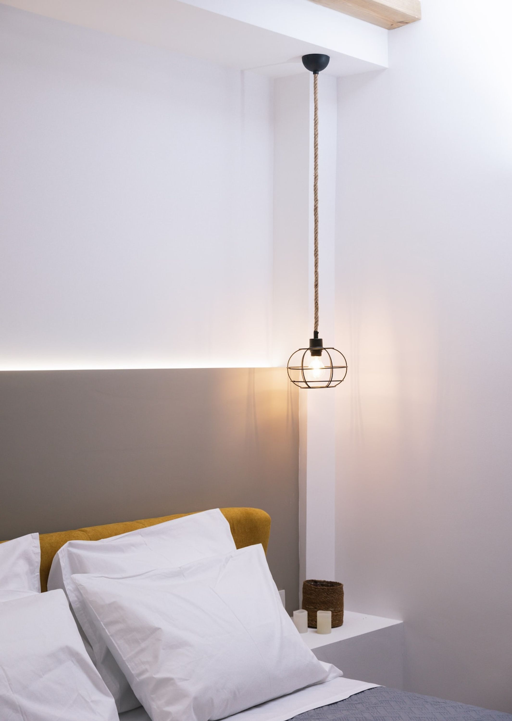 Una cama con ropa de cama blanca, cabecera amarilla y mesita de noche con un taburete pequeño.