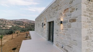 A stone building with a flat roof, a glass door, and a paved area with plants. - Ramo Dolivo Villa With Private Pool (Faistos)