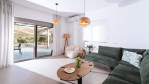 A modern living room with a sofa, a coffee table, and a view of a pool and outdoor area. - Ramo Dolivo Villa With Private Pool (Faistos)