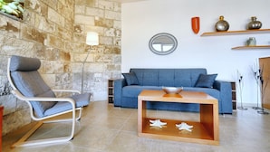 A modern living room with a stone wall, a blue sofa, a wooden coffee table, and a grey armchair. - Eleni Sea Luxury Apartment (Malevizi)