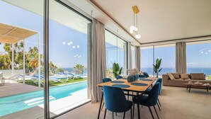 A modern interior with a dining area, a sofa, and a view of a pool and ocean. - LUX NEW Villa C with priv heated pool, ocean view (Costa Adeje)