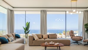 A modern living room with a sofa, armchair, and coffee table, large windows with a view of the sea, and a ceiling light fixture. - LUX NEW Villa C with priv heated pool, ocean view (Costa Adeje)