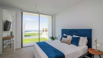 A bedroom with a bed, a TV, a desk, and a view of the outdoors.