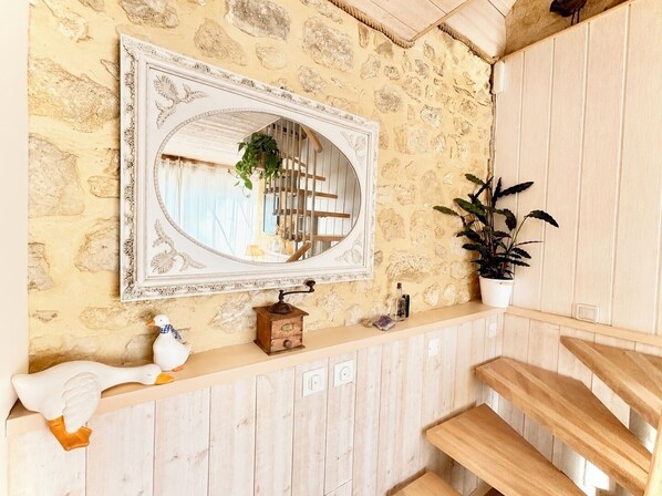 Ein rustikales Interieur mit einer Steinsäule, einer Holztreppe, einem spiegelnden, weiß umrahmten Spiegel, einer Holzkiste und einem Blumentopf.