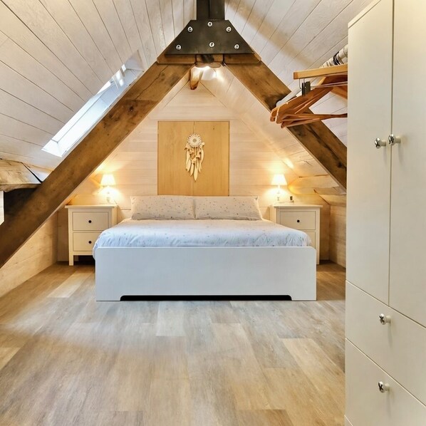 A bedroom with a sloped ceiling, a bed, bedside tables, and a wardrobe.